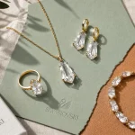 Bijoux Swarovski femme : collier, bague et boucles scintillants sur fond lin beige